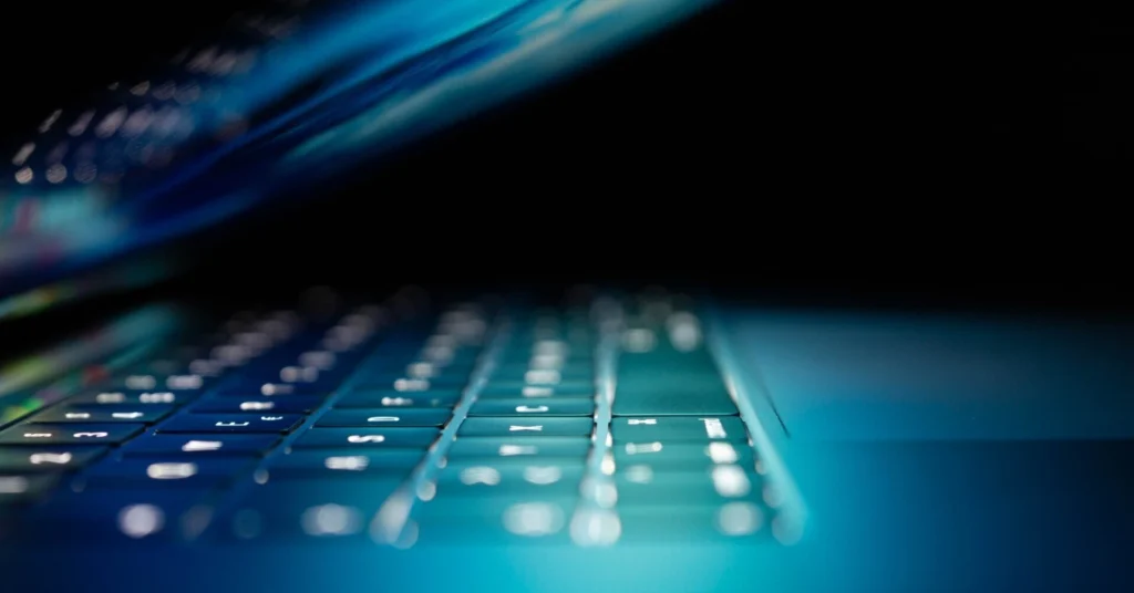 Close-up of a laptop keyboard illuminated by blue light.